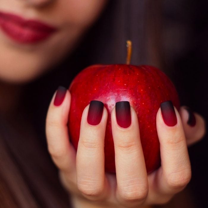 Uñas rojo con negro sosteniendo una manzana 