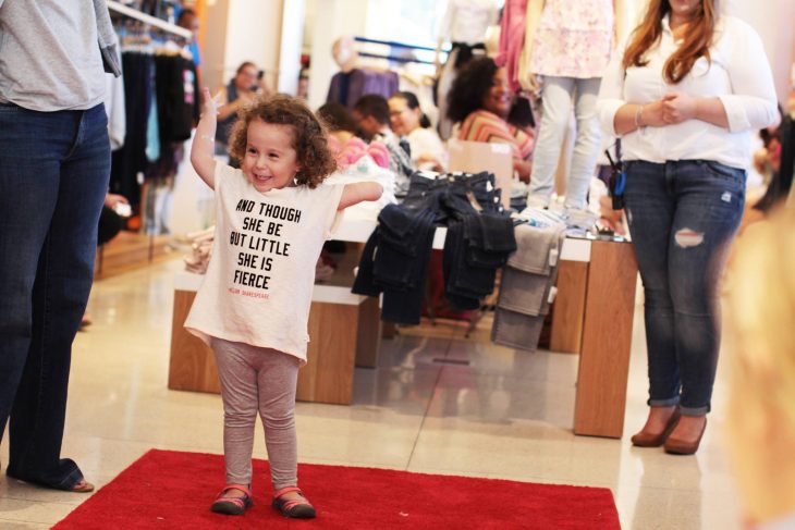 Niña que no tiene un brazo parada sobre una alfombra roja en una tienda 