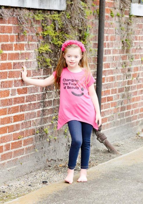 Niña usando una camisa rosa mientras está recargada en una pared 