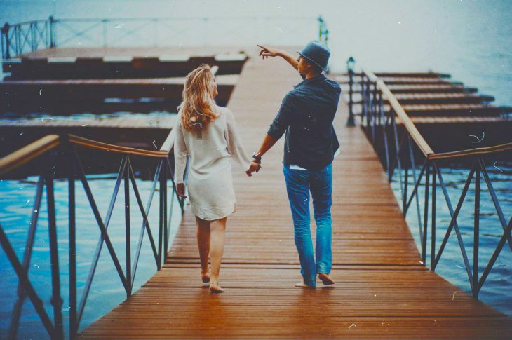 Pareja de novios tomados de las manos caminando por un muelle 