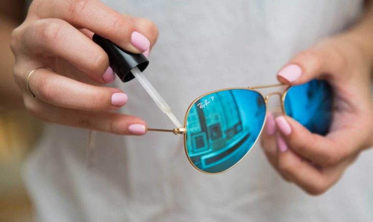 Chica colocándole esmalte de uñas transparente a unos lentes 