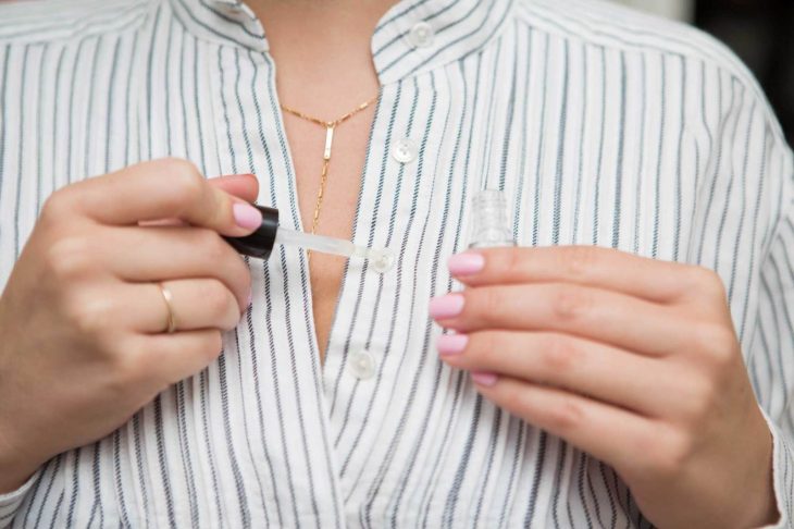 Mujer untandole esmale transparente de uñas a un botón