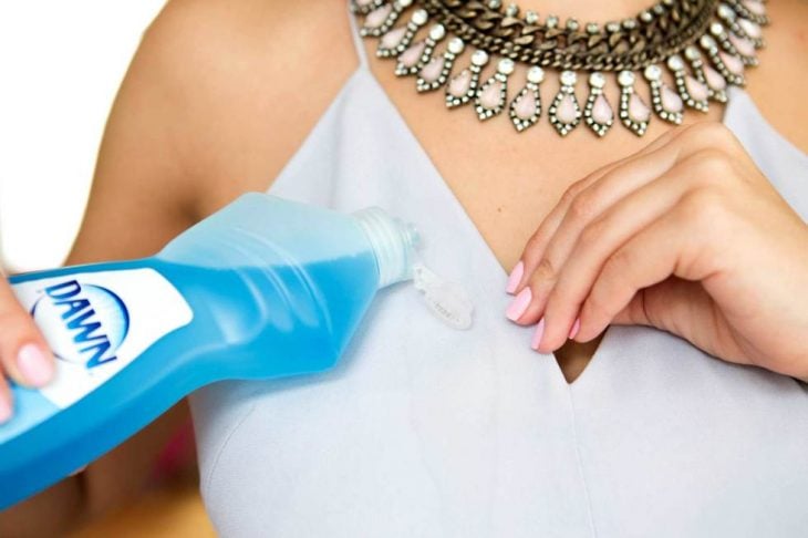Mujer poniendo detergente liquido sobre su blusa manchada con grasa