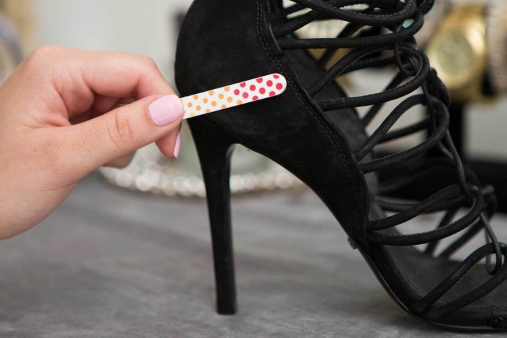 Chica eliminando las peluzas de unos zapatos de gamuza con una lima de uñas