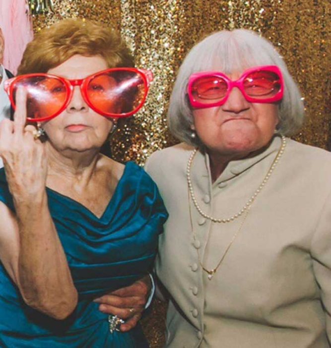 abuelitas en una cabina de fotos con lentes enormes y mostrando su dedo corazón 