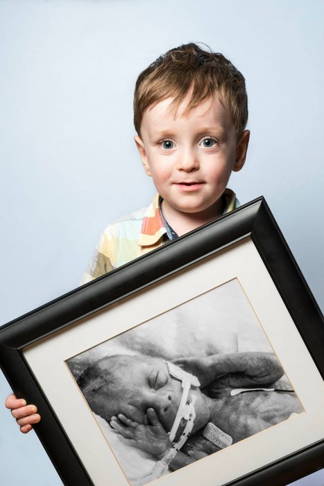 Niño sosteniendo un cuadro con una foto de el cuando era un bebé prematuro