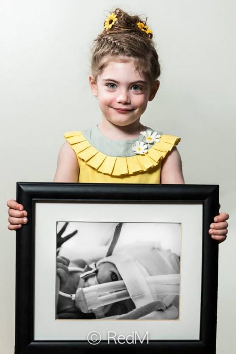 Niña vestida de amarillo sosteniendo una imagen de ella cuando era bebé y estaba en la incubadora