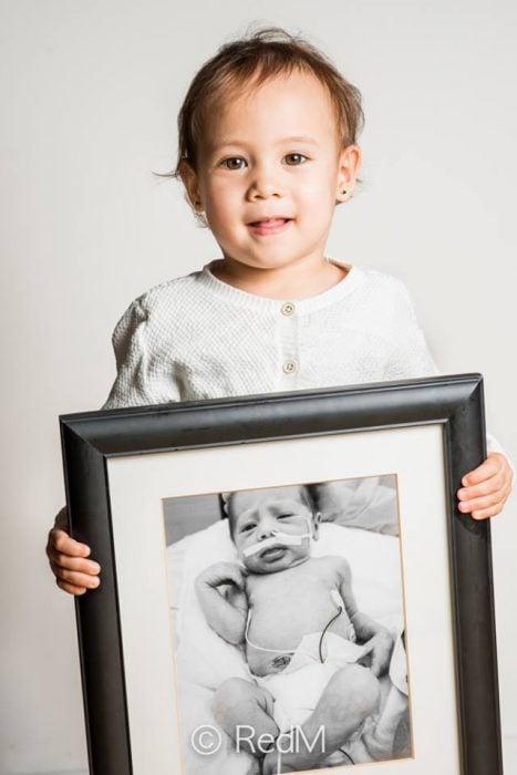 bebé sosteniendo una imagen de ella cuando era una bebé prematura 