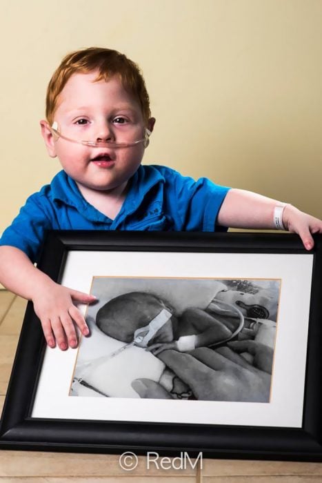 niño sosteniendo un cuadro de él mismo cuando era un bebé prematuro