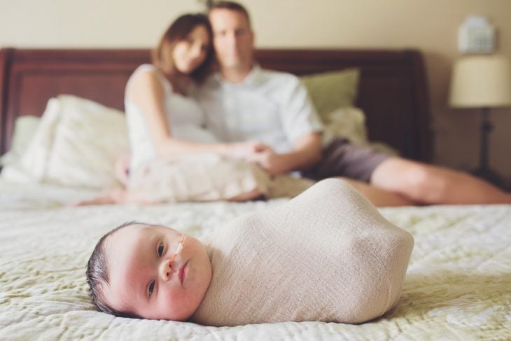 sesión de fotos de una bebé que nació con un tumor en el cerebro y síndrome de down recostada en una cama 