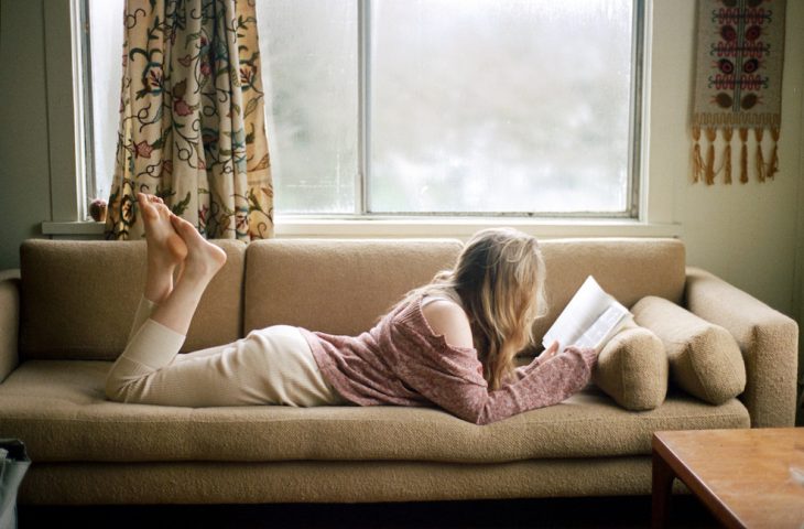 Chica recostada en un sofá leyendo un libro 