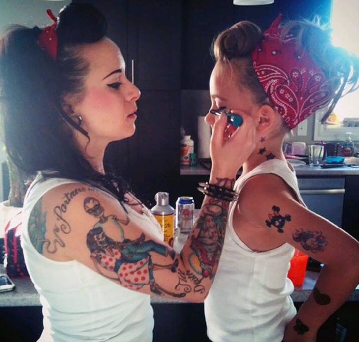 chica tatuada maquilla a niña pequeña