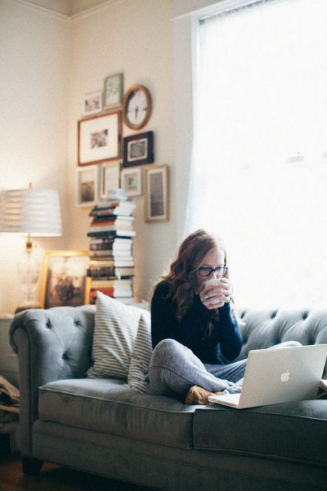 Chica bebiendo café mientras trabaja con su laptop en el sofá