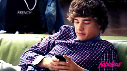 GIF chico que está sentado en el sofá con el celular en las manos
