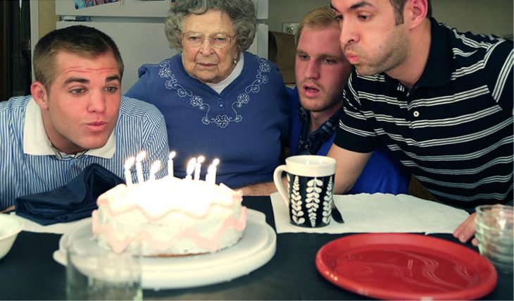 Hombres soplando una vela de cumpleaños en un pastel acompañados de su abuela 