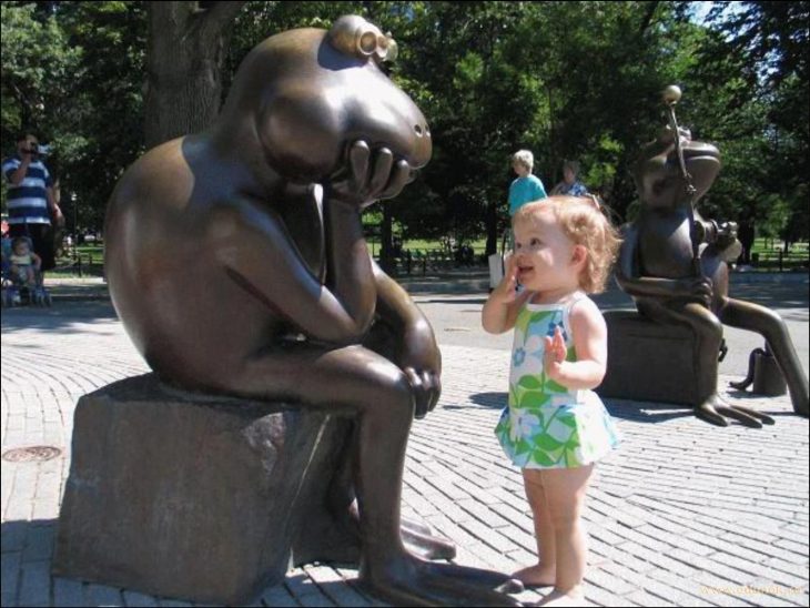 Niña viendo con una mano en la boca a una estatua en forma de rana 