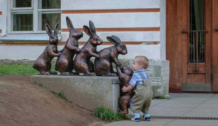 Niño formado atrás de unos conejos como estatua 
