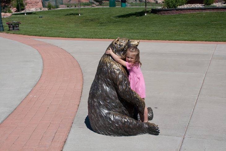 Niña abrazando a una estatua en forma de oso 