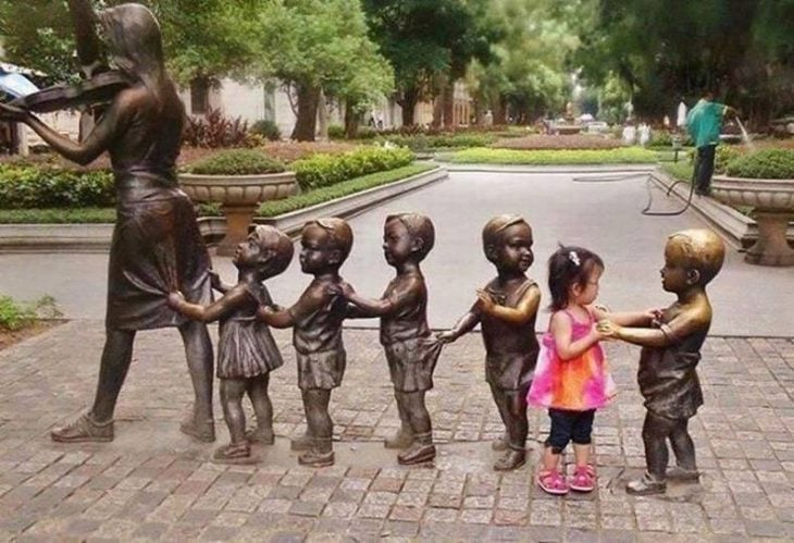 niña intentando jugar con varias estatuas de niños