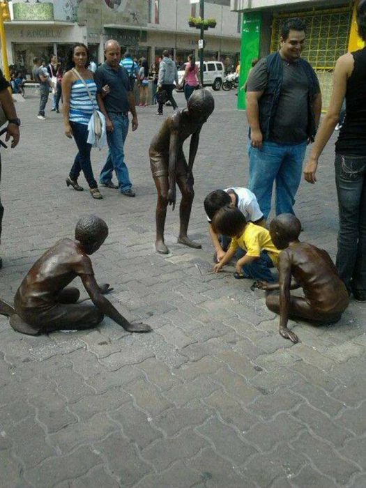 Niños jugando en el suelo junto a unas estatuas