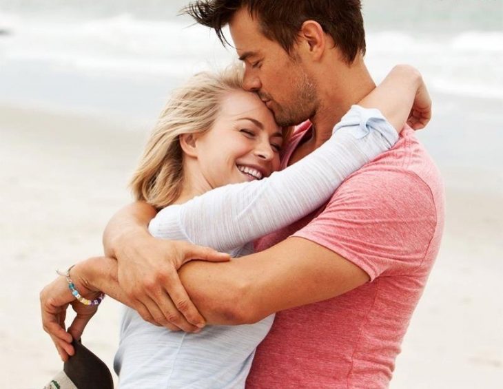 Pareja de novios abrazados sonriendo mientras están en la playa