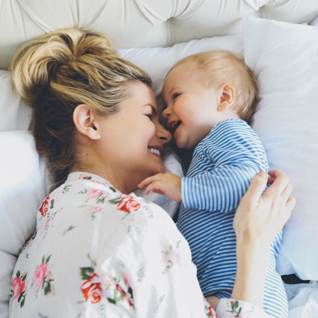 mamá junto a su bebé sonriendo mientras están recostados en la cama 