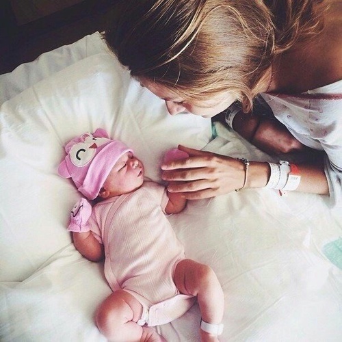 Madre tomando la mano de su bebé que esta recostado en la cama 