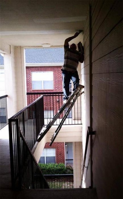 Hombre sobre una escalera colocada al vacio intentando cambiar un foco