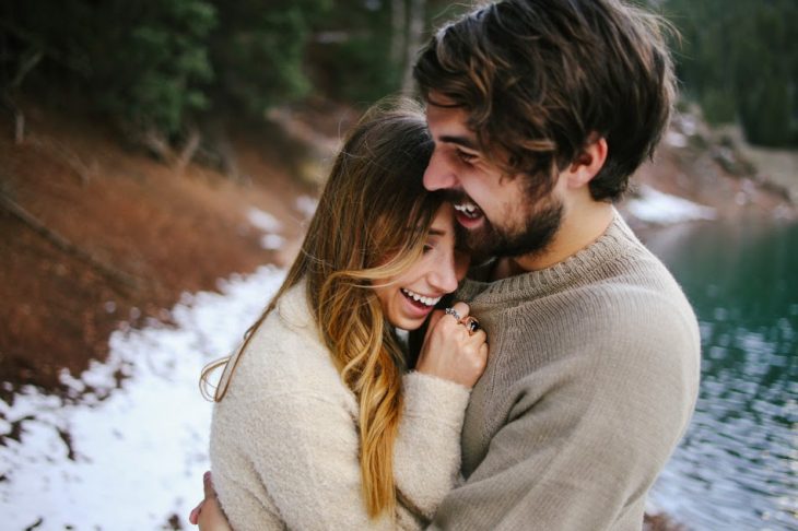 Pareja de novios abrazados tiendo mientras están en la nieve 