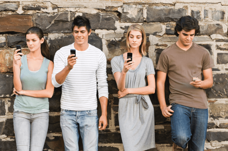 Grupo de chicos recargados en una pared con celulares en las manos 