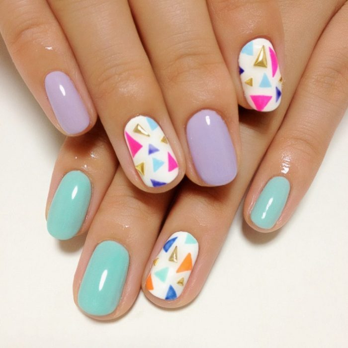 Uñas decoradas con esmalte color azul y lila y pequeñas piedras de colores 