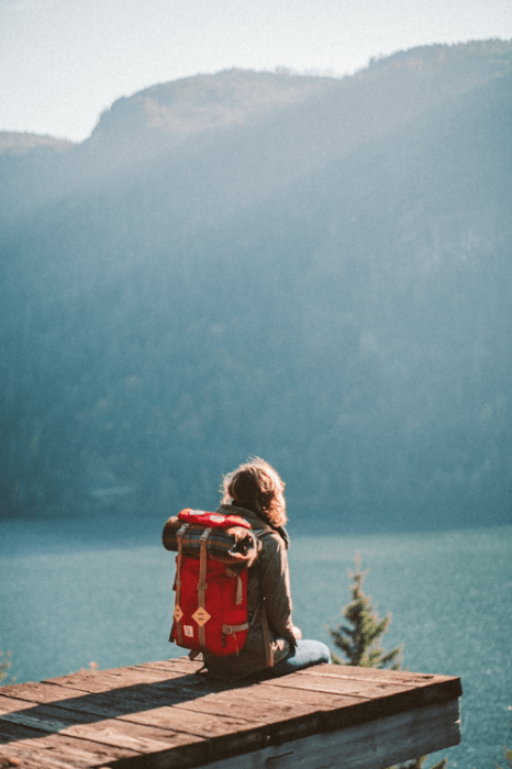 chica con mochila sentada frente a un lago