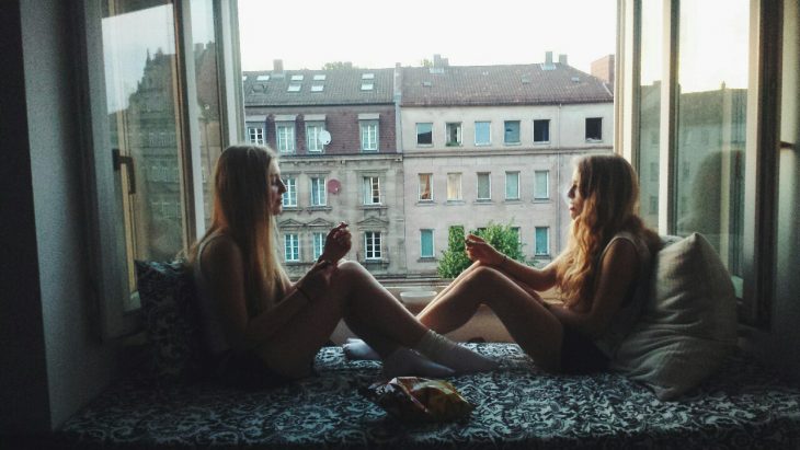 Mejores amigas sentadas frente a una ventana conversando 