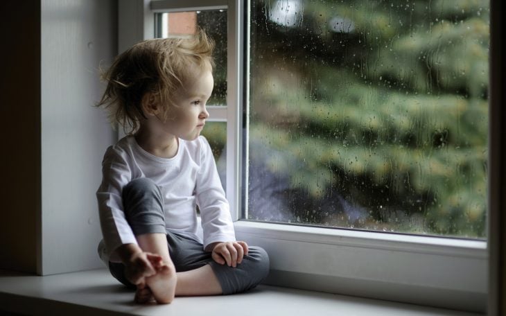 Bebé sólo sentado cerca de la ventana viendo el jardín 