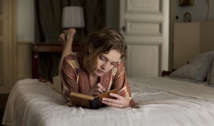 Chica recostada en una cama escribiendo en un libro 