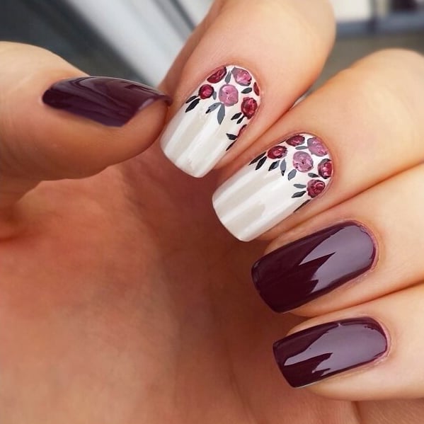 Uñas de color ciruela con diseños de flores en color blanco 