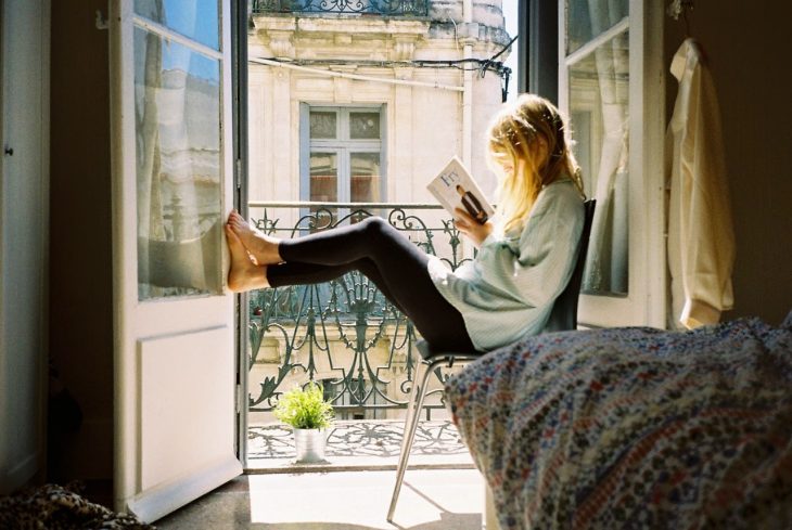 Chica sentada junto a una ventana leyendo un libro 