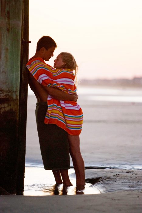 Pareja de novios abrazados mientras están en la playa disfrutando del atardecer 