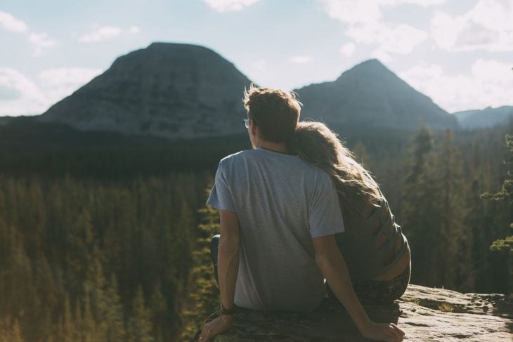 Pareja de novios sentados en una roca en las montañas viendo el horizonte 