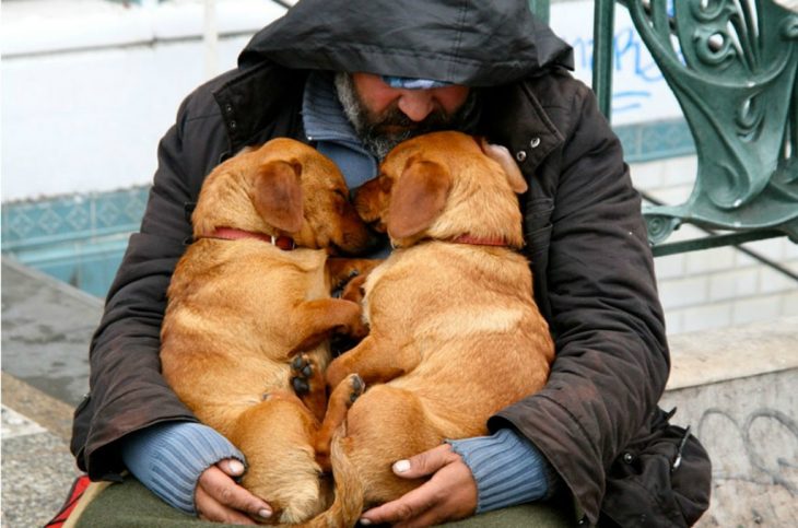 persona indigente abrazando a sus dos perros 