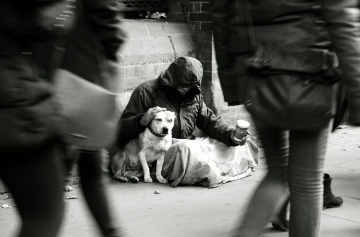 Persona pidiendo limosna y acariciando a su perro 