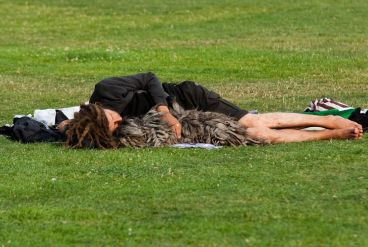 Chico con rastas acostado en el pasto con su perro 