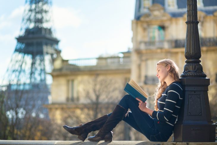 Chica recargada en un poste leyendo 