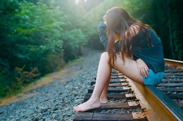 Chica sentada sobre las vías del tren tomándose la cabeza y pensando