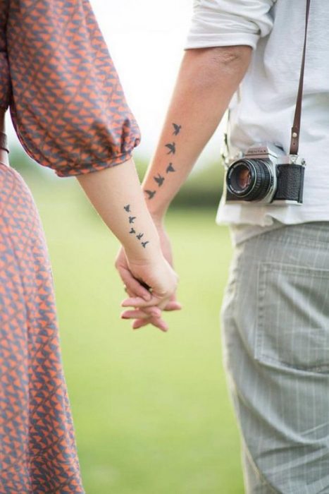 pareja tomados de las manos mostrando sus tatuajes de pájaros 