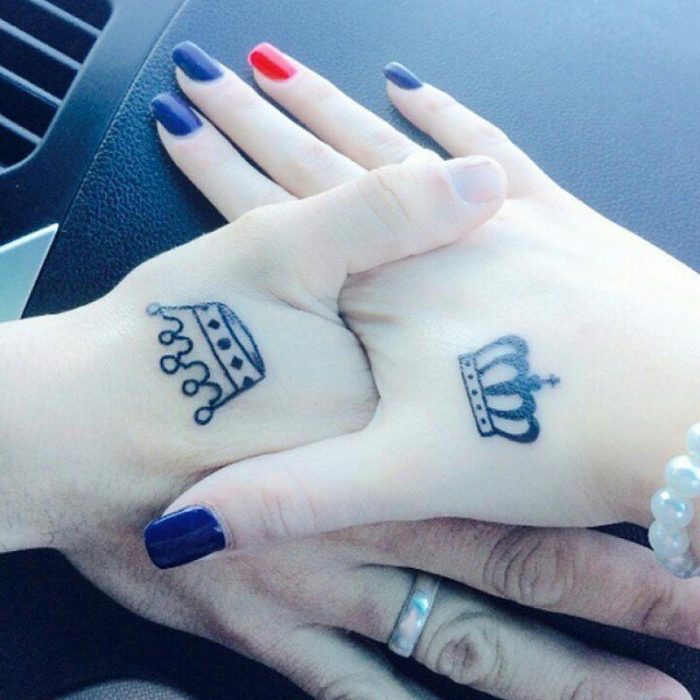 pareja tomados de las manos mostrando su tatuaje de coronas 