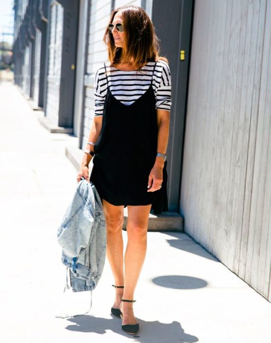 Chica caminando por la calle mientras usa un vestido negro largo con camisa debajo