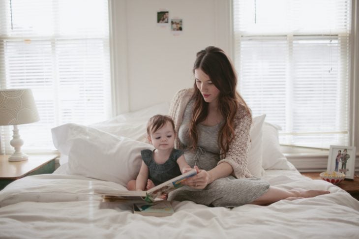Mujer sentada en la cama leyendole un cuento a una bebé