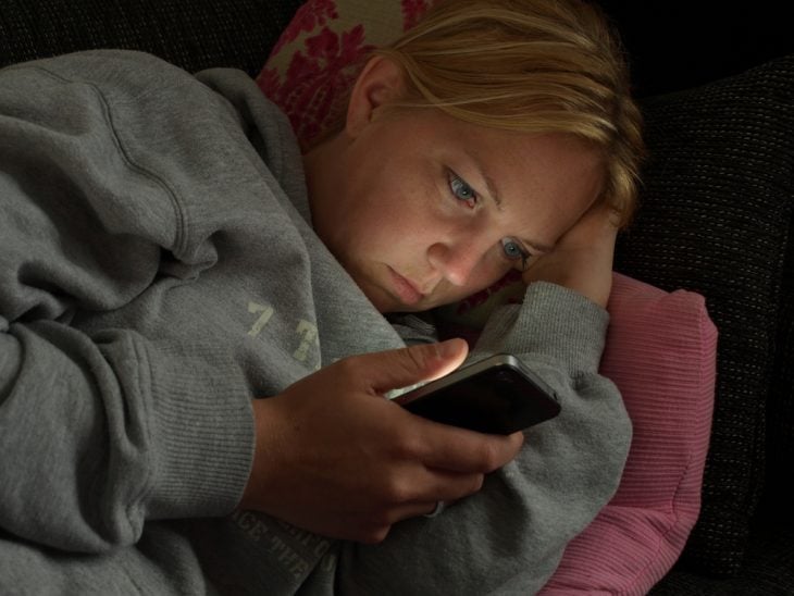Chica recostada en su cama viendo su celular 