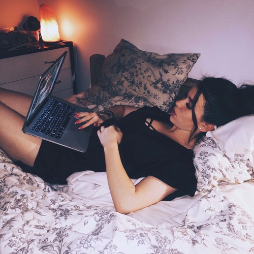 Chica recostada en una cama con la computadora en las piernas 